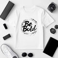 Be Bold unisex white t-shirt with a bold graphic design, surrounded by stylish accessories on a flat lay background.