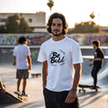 Young man wearing Be Bold unisex white t-shirt at a skate park, exuding confidence and style among friends.