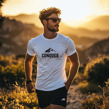 Man wearing Conquer Men's White T-shirt against a sunset backdrop, showcasing style and confidence outdoors.